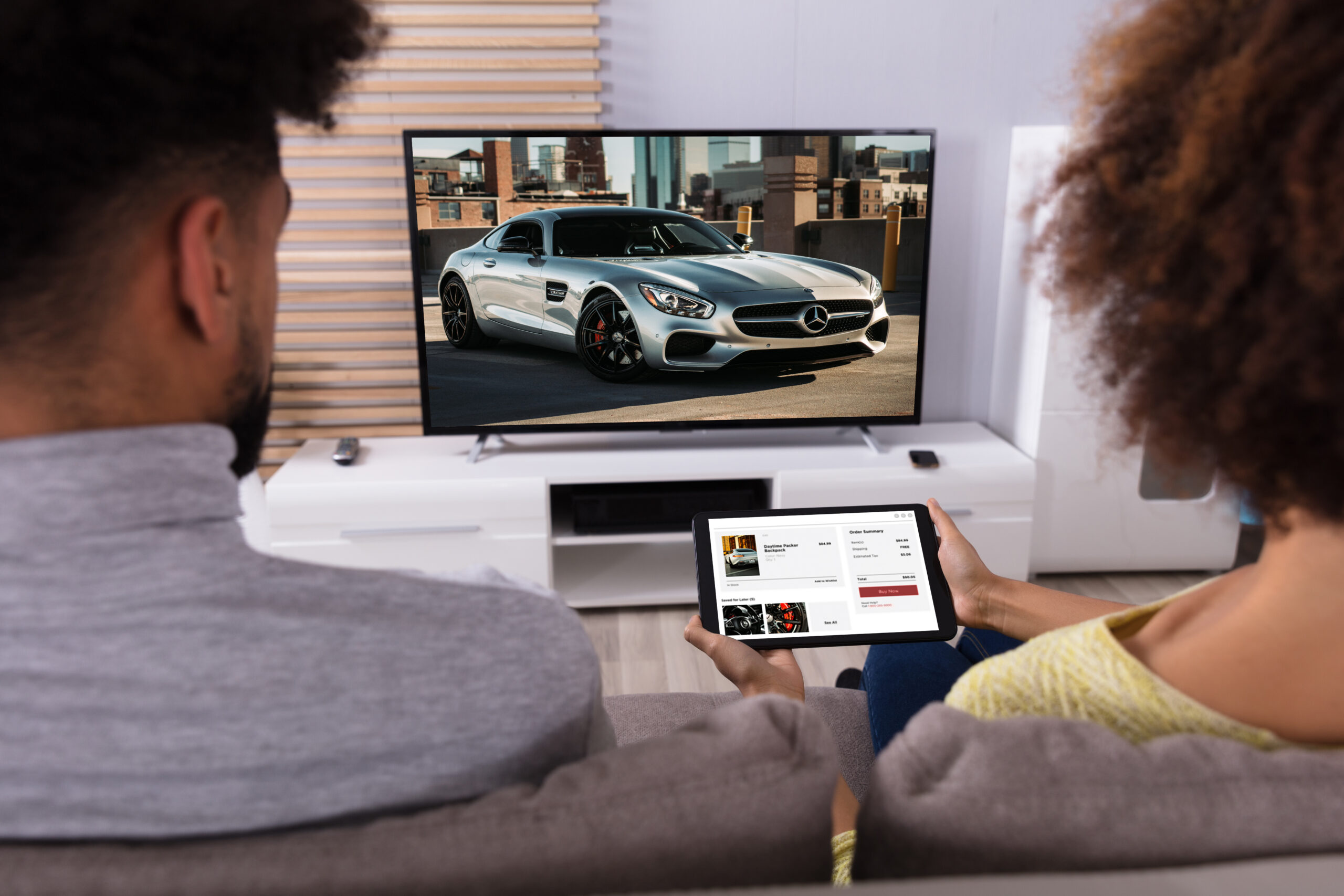 Young Couple Sitting On Sofa Connecting Television Channel Through WiFi On Digital Tablet